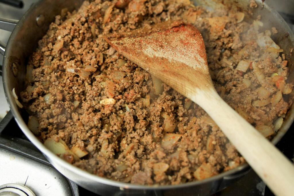 Adding spices to the ground beef in a sauté pan.