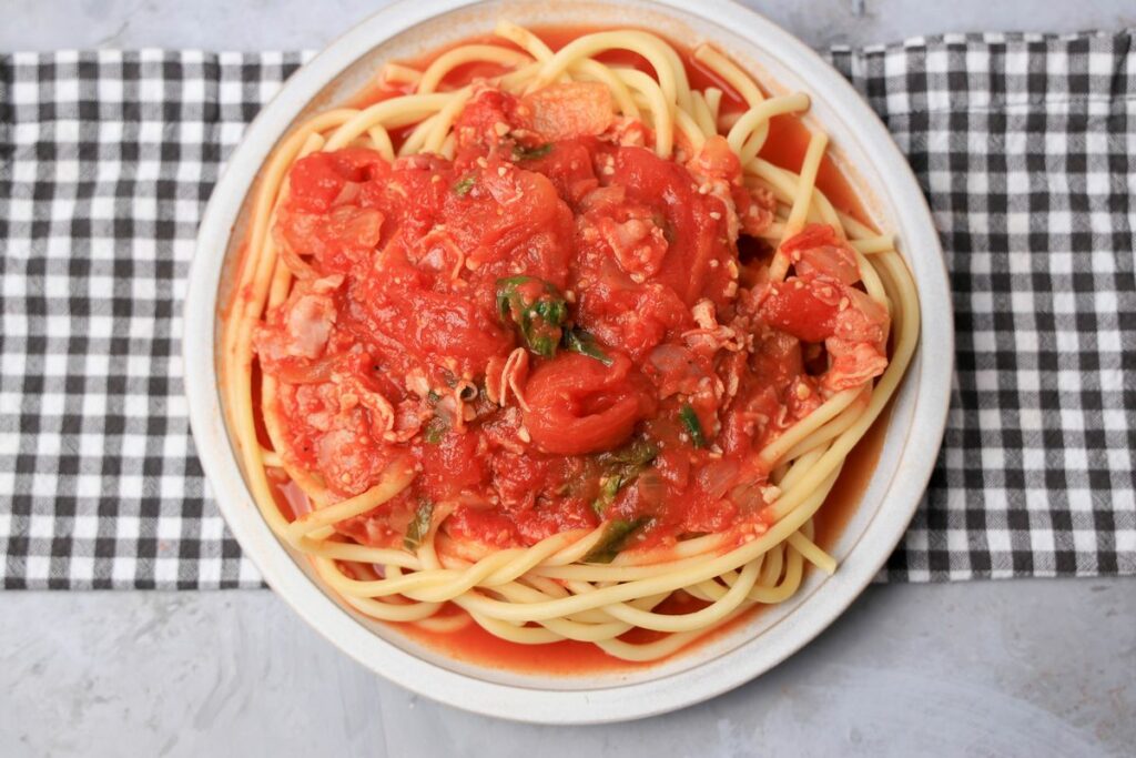 Bucatini All'Amatriciana on a stone plate with a gray plaid napkin.