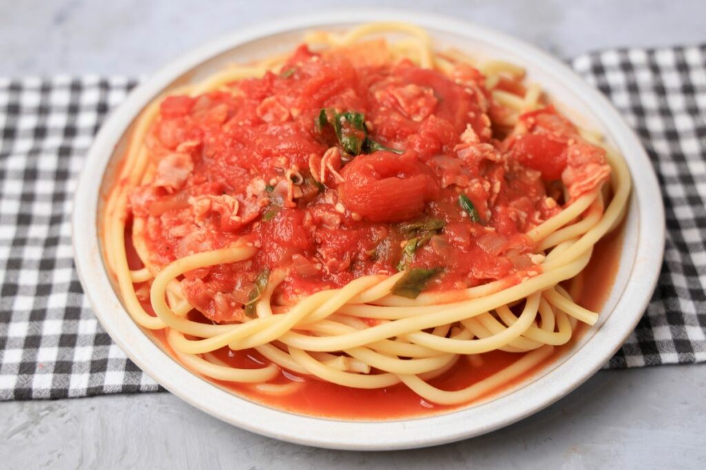 Bucatini All'Amatriciana on a stone plate with a gray plaid napkin.