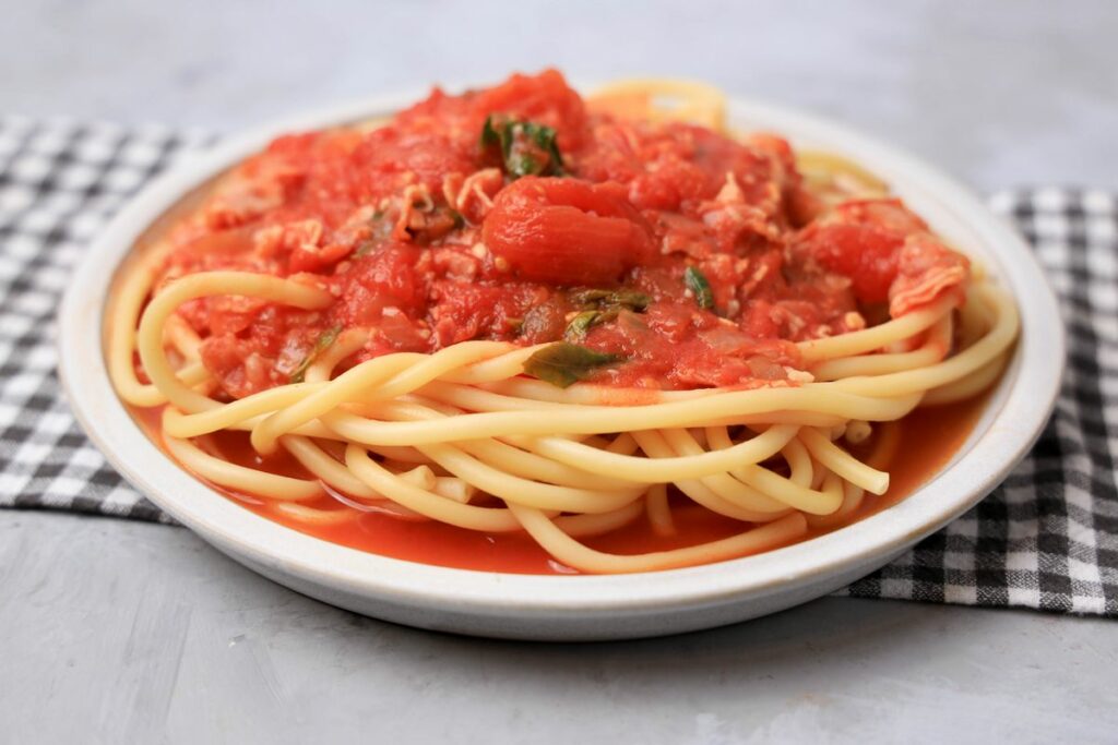 Bucatini All'Amatriciana on a stone plate with a gray plaid napkin.