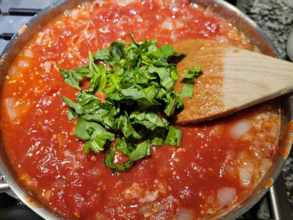 Panetta, garlic, and onion with peeled tomatoes and basil in a sauce pan.