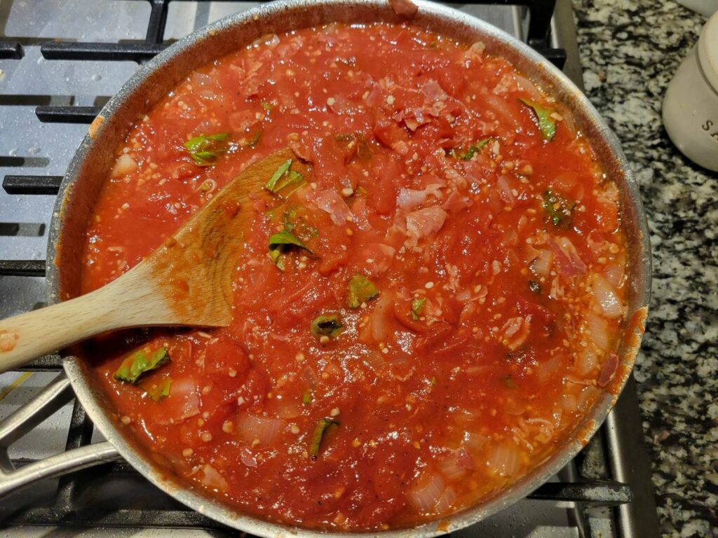 Panetta, garlic, and onion with peeled tomatoes and basil in a sauce pan.