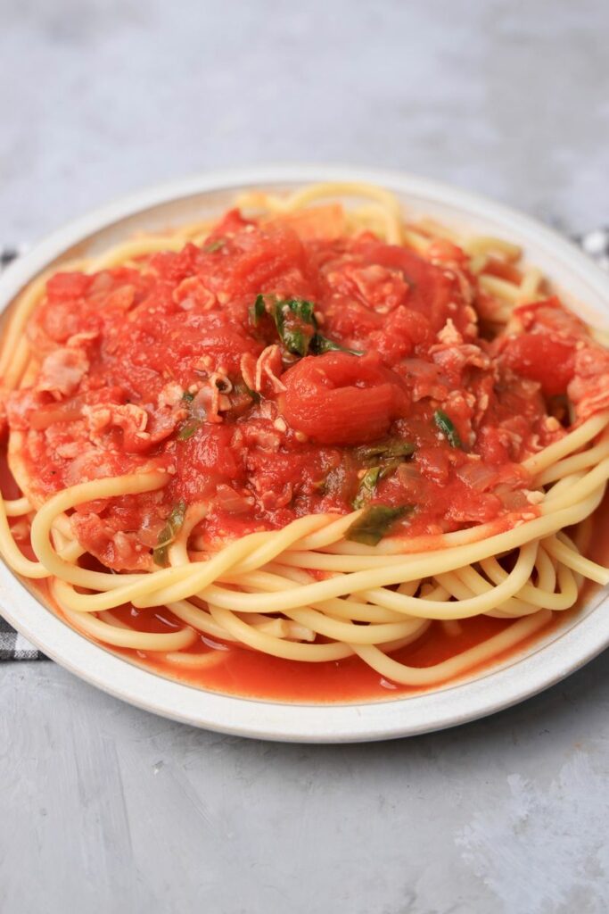 Bucatini All'Amatriciana on a stone plate with a gray plaid napkin.