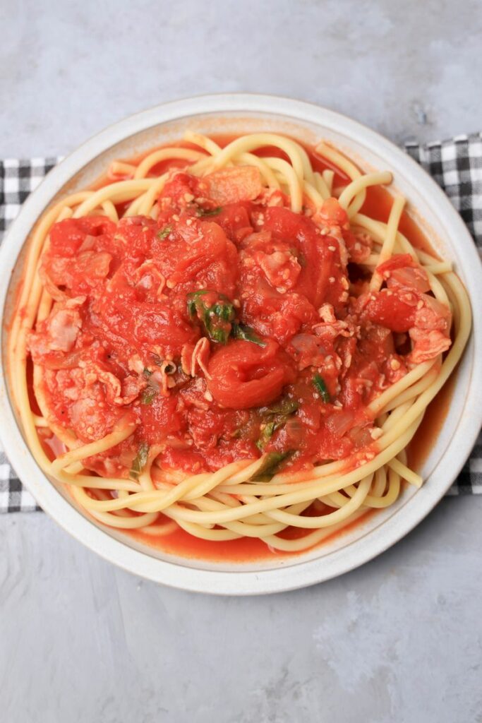 Bucatini All'Amatriciana on a stone plate with a gray plaid napkin.