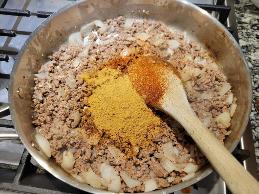 Ground beef, onion, and spices inside a pan.