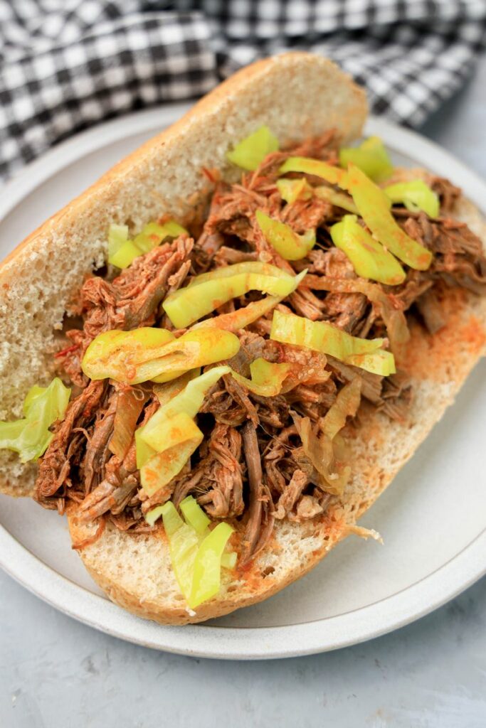 Slow cooker Italian beef sandwich on a stone plate on faux concrete backdrop.