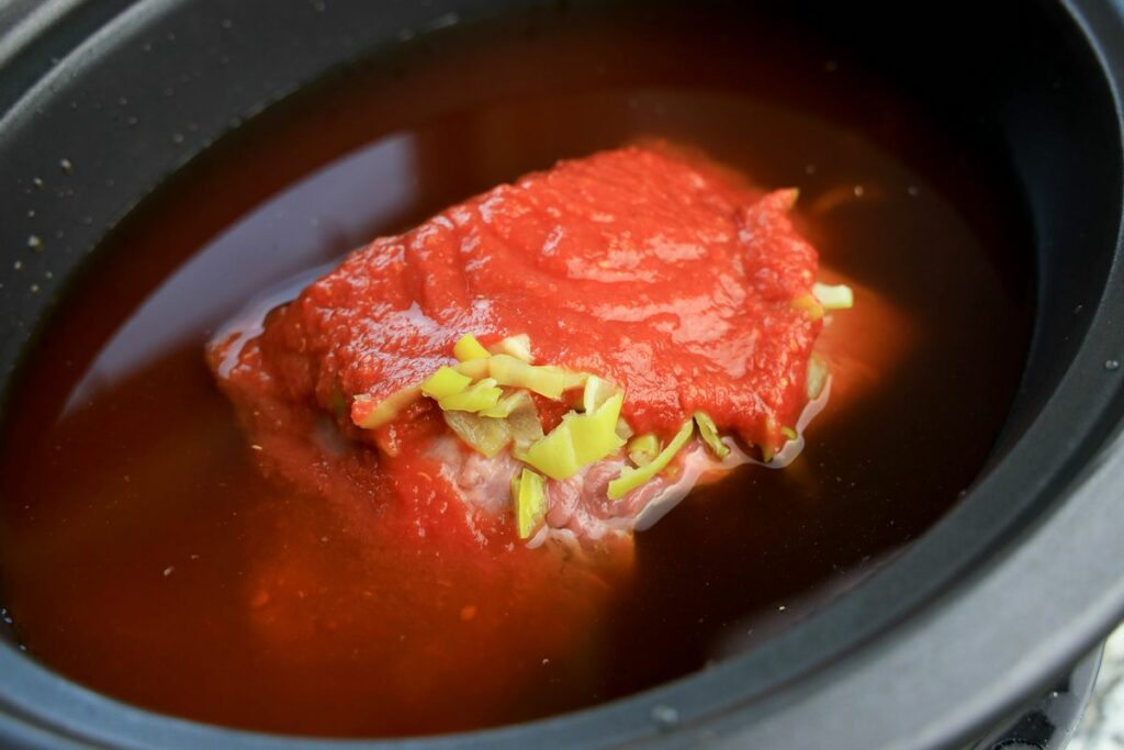 Beef roast in beef broth, crushed tomatoes, and pepperoncini juice in a slow cooker.