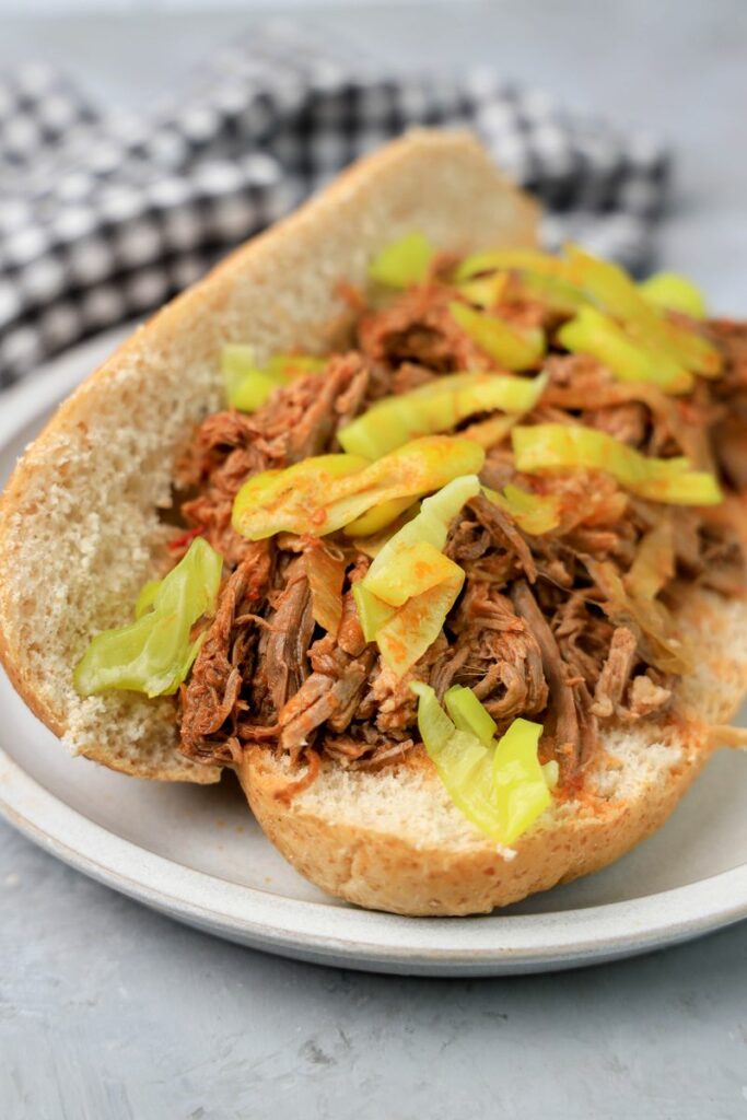 Slow cooker Italian beef sandwich on a stone plate on faux concrete backdrop.