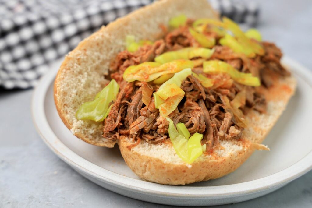 Slow cooker Italian beef sandwich on a stone plate on faux concrete backdrop.