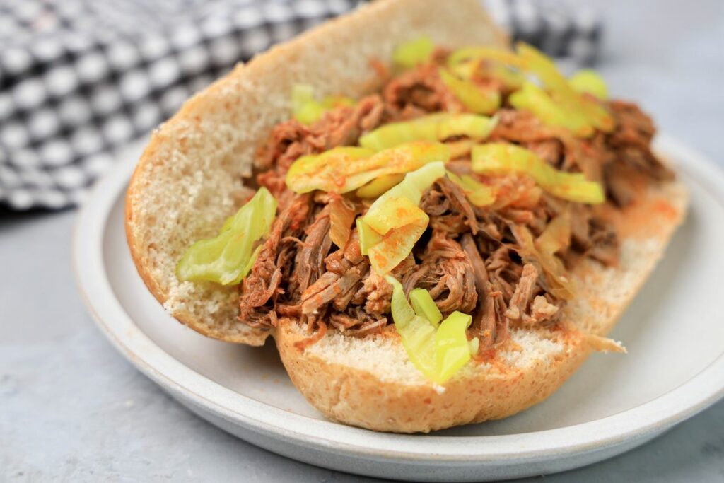 Slow cooker Italian beef sandwich on a stone plate on faux concrete backdrop.