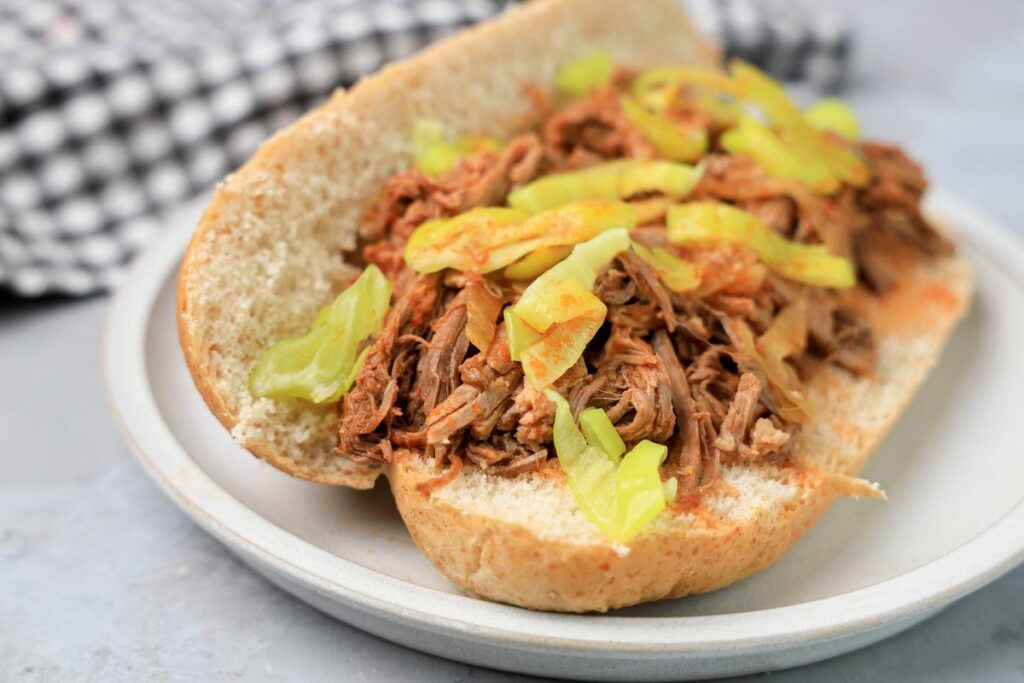 Slow cooker Italian beef sandwich on a stone plate on faux concrete backdrop.