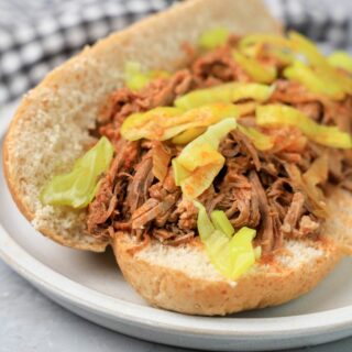 Slow cooker Italian beef sandwich on a stone plate on faux concrete backdrop.