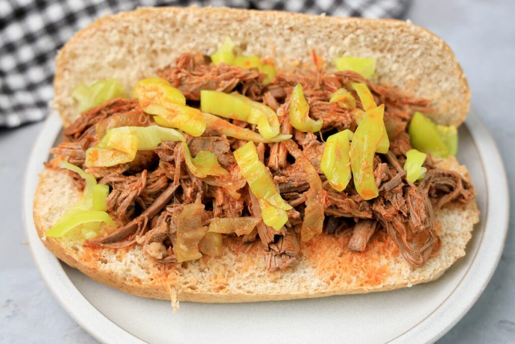 Slow cooker Italian beef sandwich on a stone plate on faux concrete backdrop.