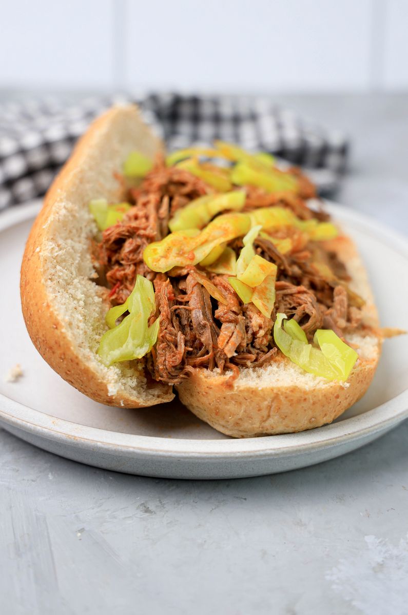 Slow cooker Italian beef sandwich on a stone plate on faux concrete backdrop.