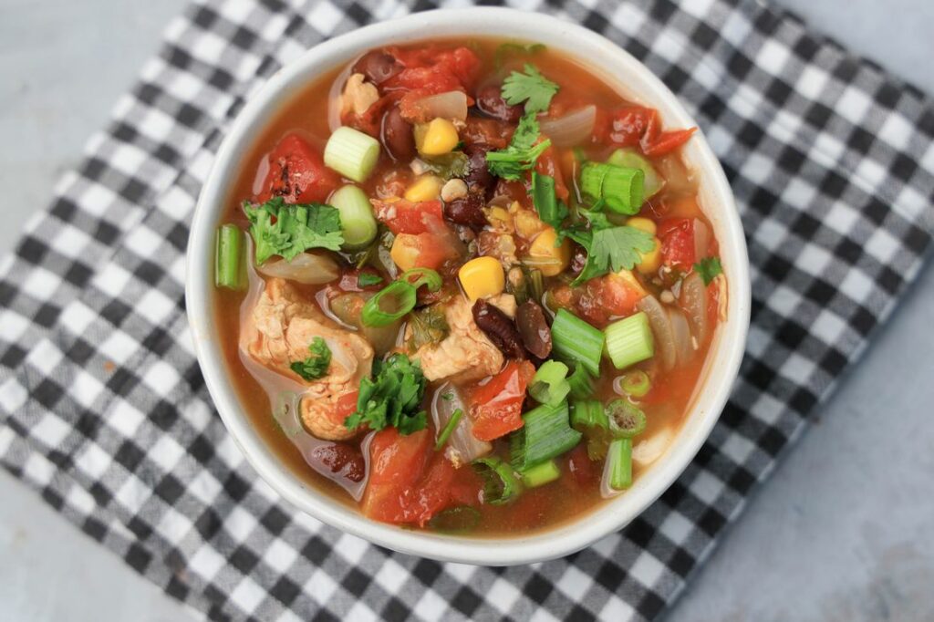 Baja Chicken Soup in a white bowl on a gray plaid napkin on a faux concrete backdrop.