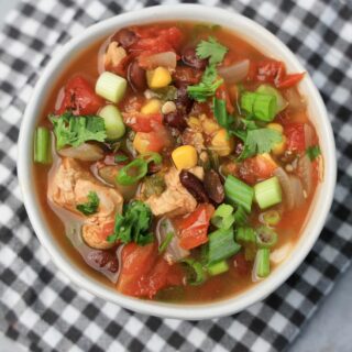 Baja Chicken Soup in a white bowl on a gray plaid napkin on a faux concrete backdrop.