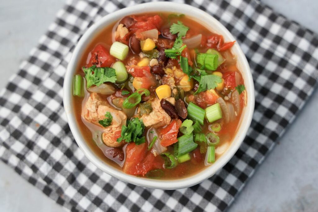 Baja Chicken Soup in a white bowl on a gray plaid napkin on a faux concrete backdrop.