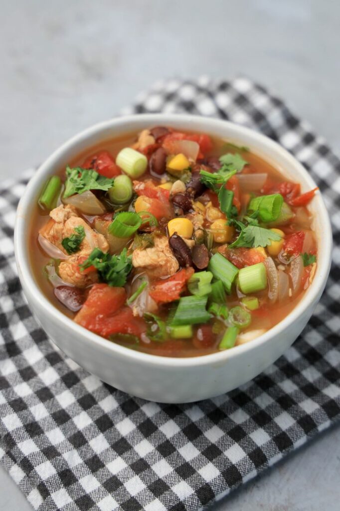 Baja Chicken Soup in a white bowl on a gray plaid napkin on a faux concrete backdrop.