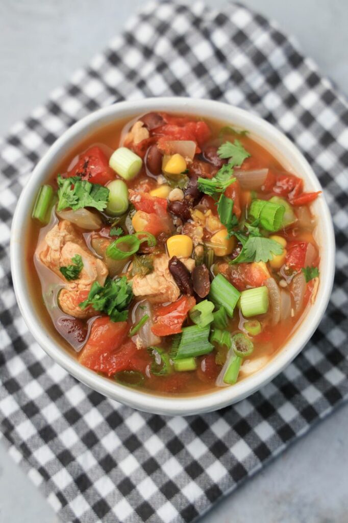 Baja Chicken Soup in a white bowl on a gray plaid napkin on a faux concrete backdrop.