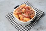 Italian Goulash with stewed tomatoes, onions, and bell pepper topped with parmesan cheese in a white bowl on a gray plaid napkin and concrete backdrop