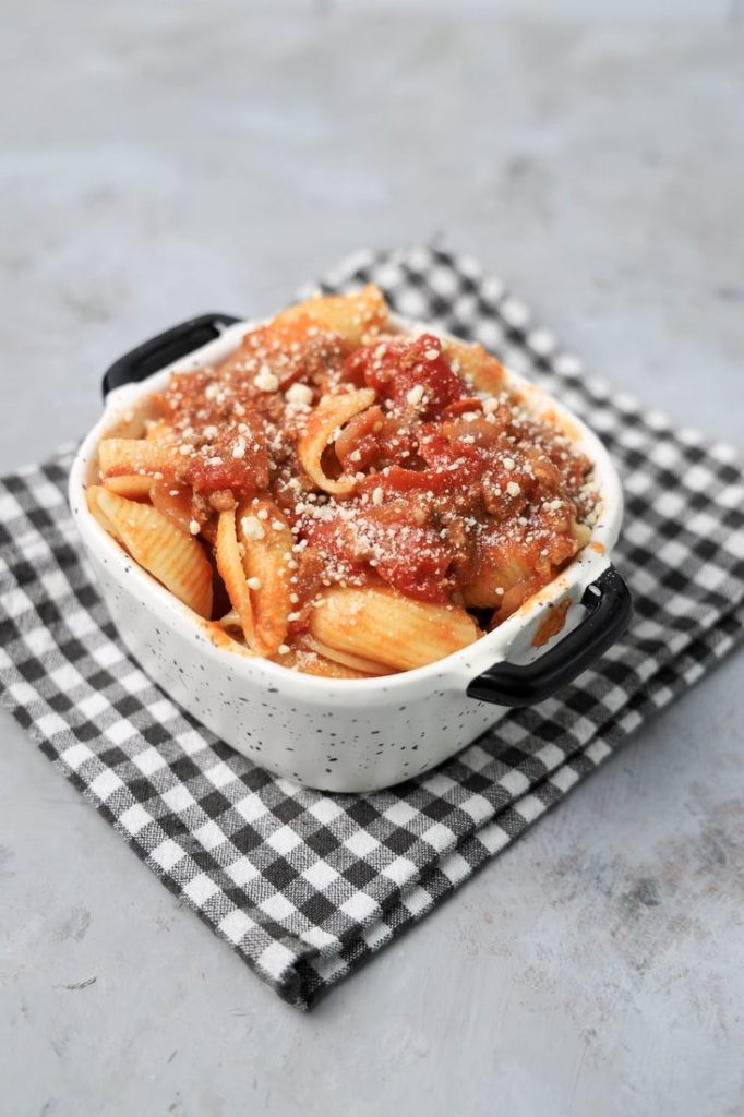 Italian Goulash with stewed tomatoes, onions, and bell pepper topped with parmesan cheese in a white bowl on a gray plaid napkin and concrete backdrop