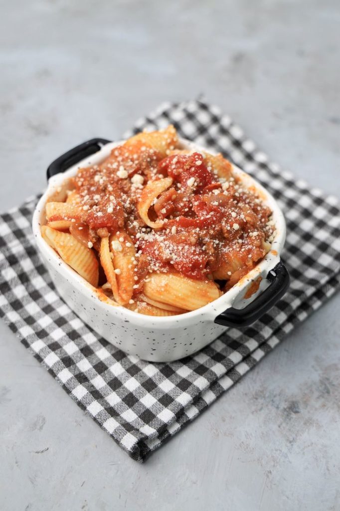 Italian Goulash with stewed tomatoes, onions, and bell pepper topped with parmesan cheese in a white bowl on a gray plaid napkin and concrete backdrop