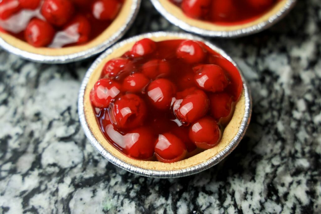 Mini pie crust filled with cherry pie filling sitting on the counter top.