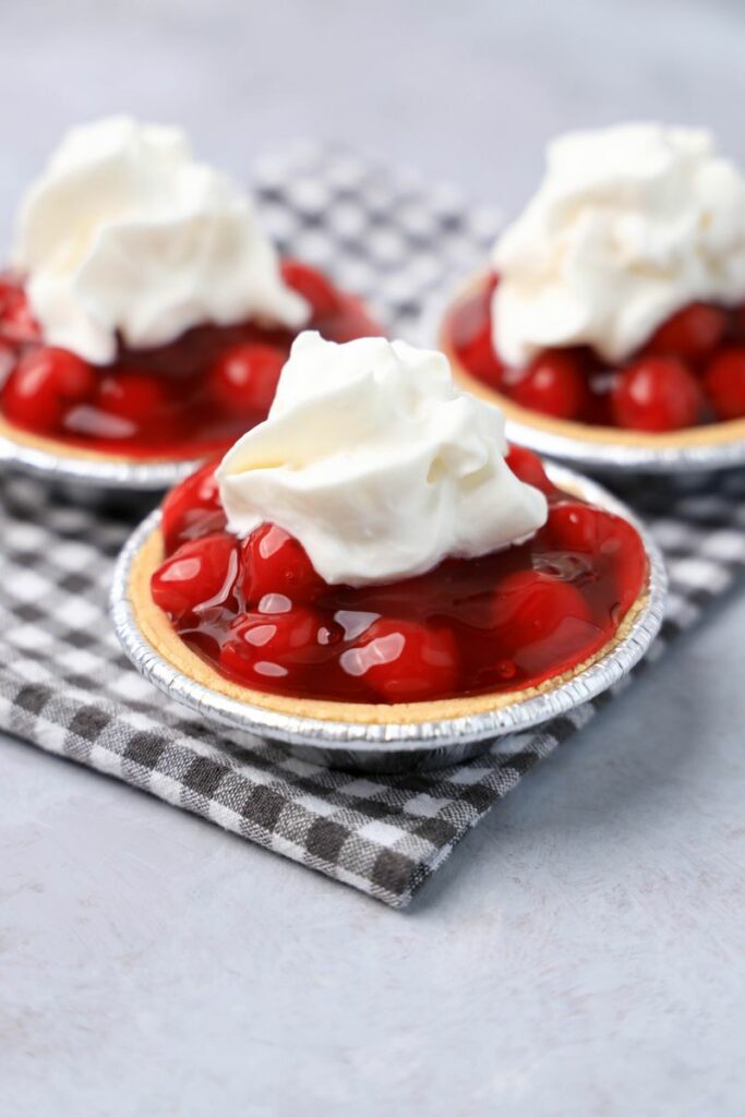 No Bake Mini Cherry Tarts on a gray plaid napkin on a faux concrete backdrop.