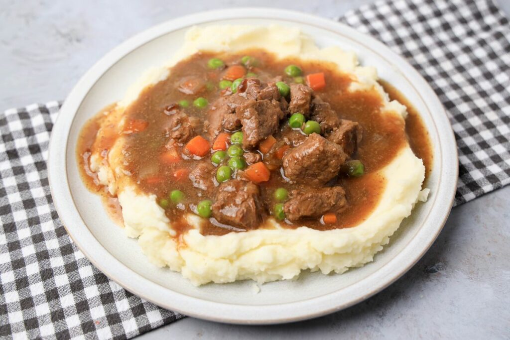 Instant Pot Irish Beef Stew plated on mashed potatoes on a stone plate with a gray plaid napkin.