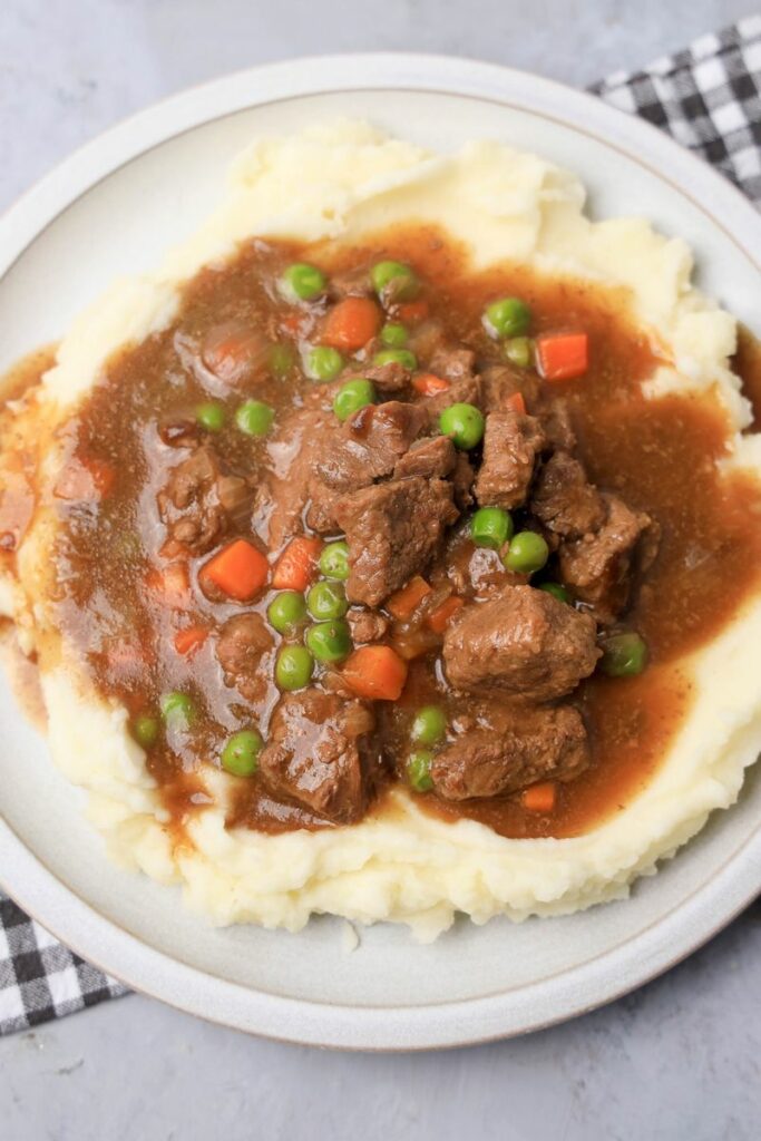 Instant Pot Irish Beef Stew plated on mashed potatoes on a stone plate with a gray plaid napkin.