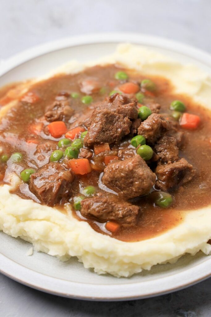 Instant Pot Irish Beef Stew plated on mashed potatoes on a stone plate with a gray plaid napkin.