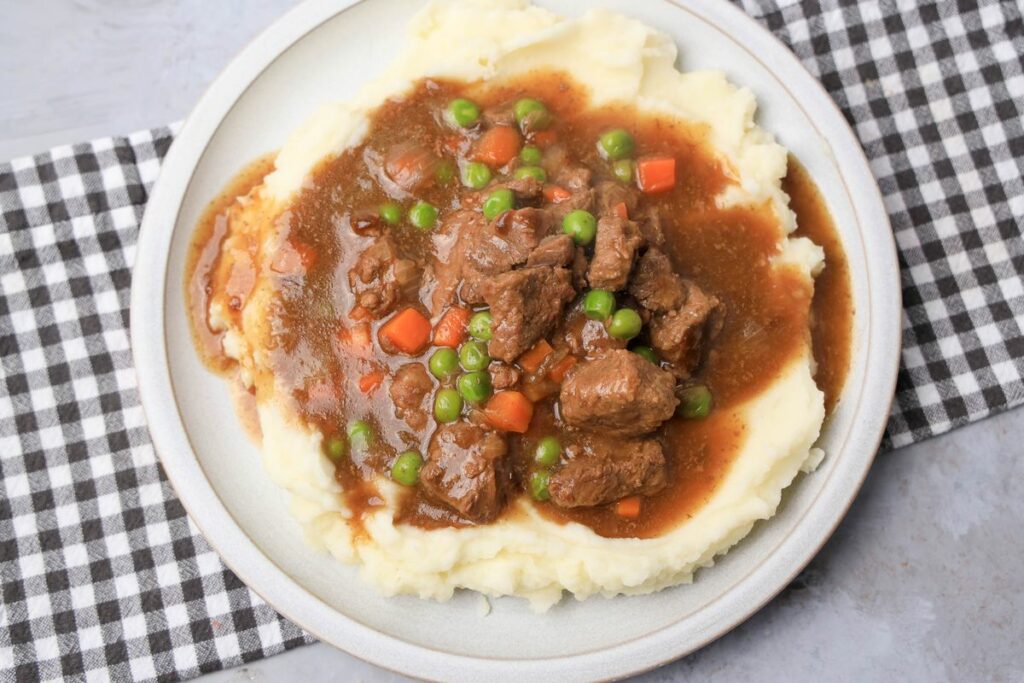 Instant Pot Irish Beef Stew plated on mashed potatoes on a stone plate with a gray plaid napkin.