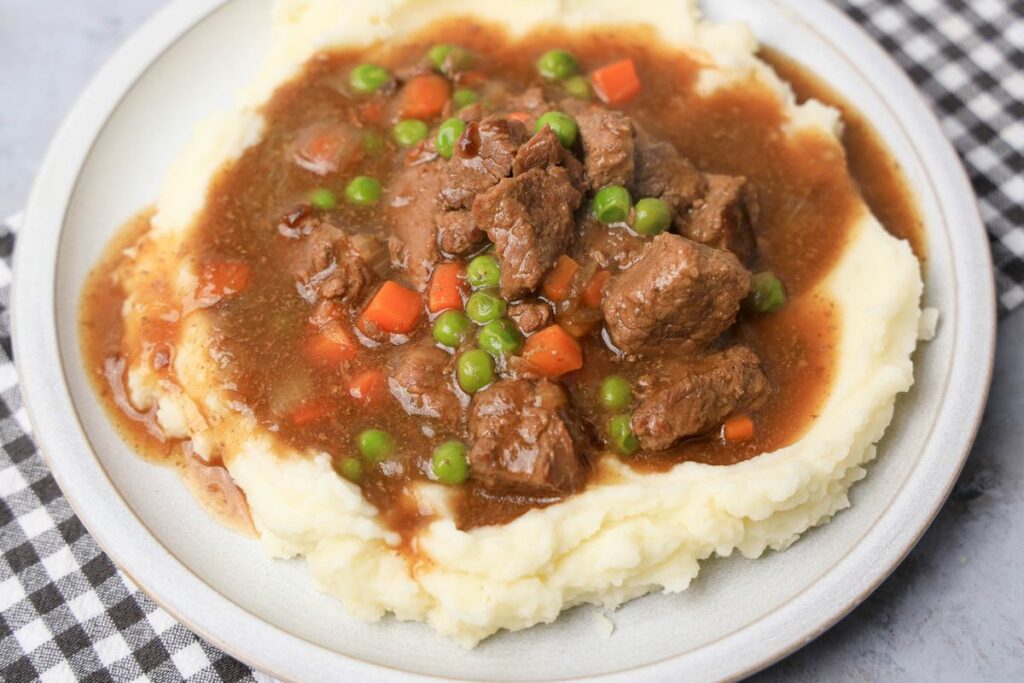 Instant Pot Irish Beef Stew plated on mashed potatoes on a stone plate with a gray plaid napkin.