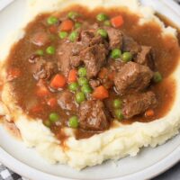 Instant Pot Irish Beef Stew plated on mashed potatoes on a stone plate with a gray plaid napkin.