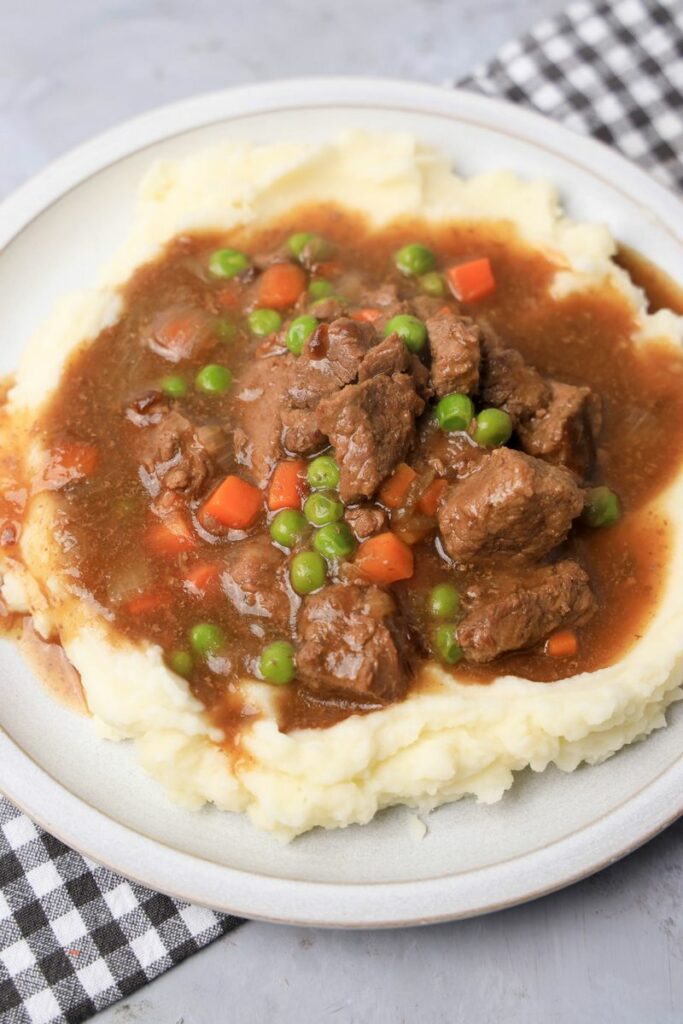 Instant Pot Irish Beef Stew plated on mashed potatoes on a stone plate with a gray plaid napkin.