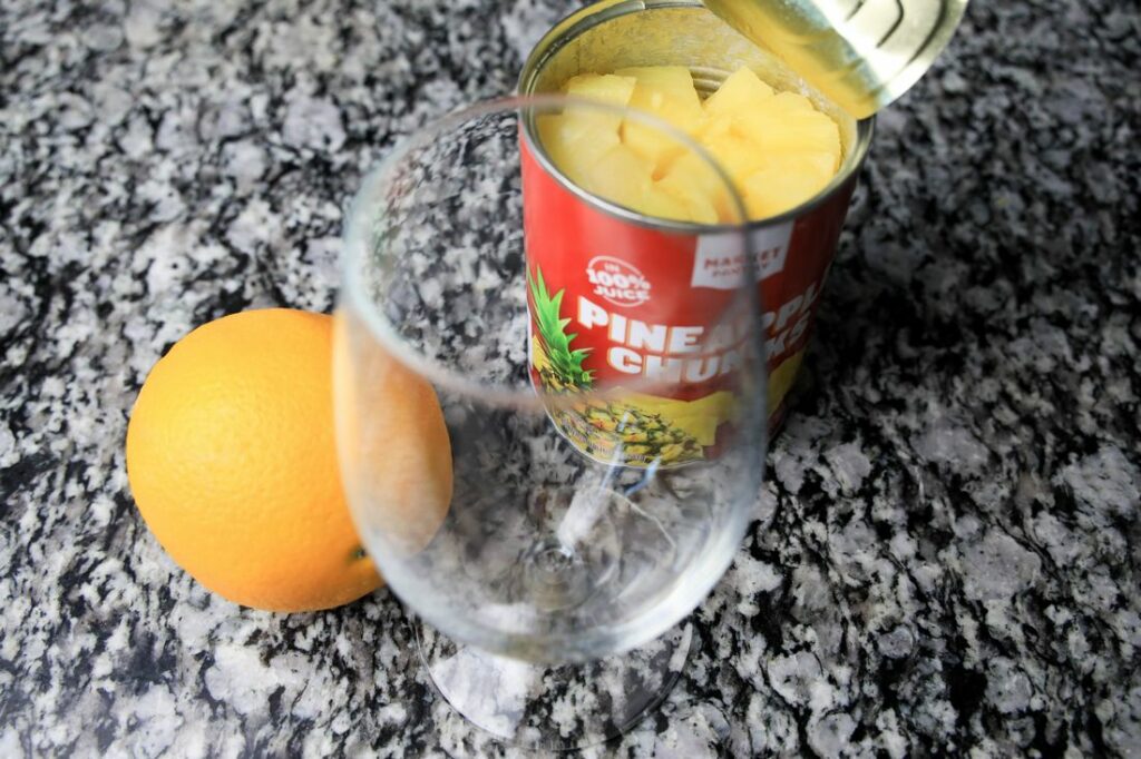 Empty glass with an orange and a can of pineapple