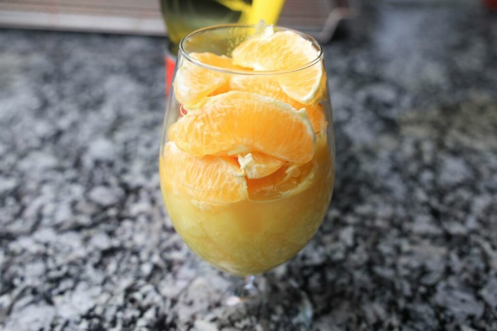 Pineapple and oranges in a glass with an open pineapple can behind it.