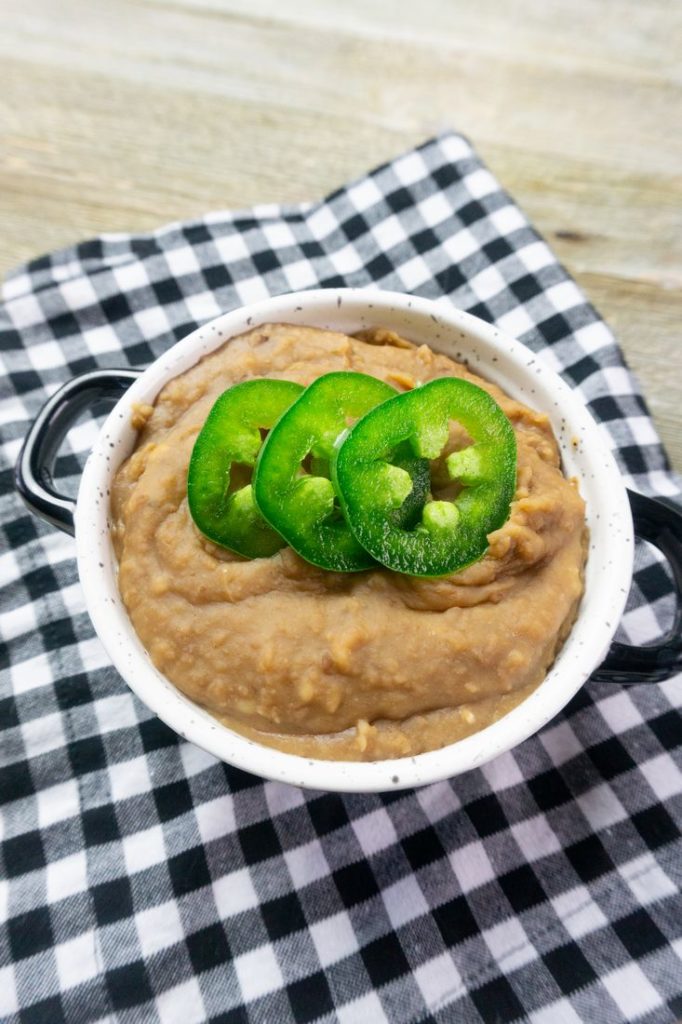 Instant Pot Refried Beans in a white bowl on plaid napkin on grey wood.