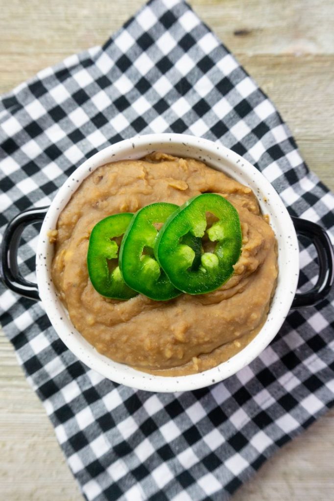 Instant Pot Refried Beans in a white bowl on plaid napkin on grey wood.