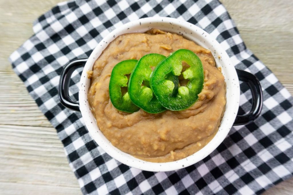 Instant Pot Refried Beans in a white bowl on plaid napkin on grey wood.