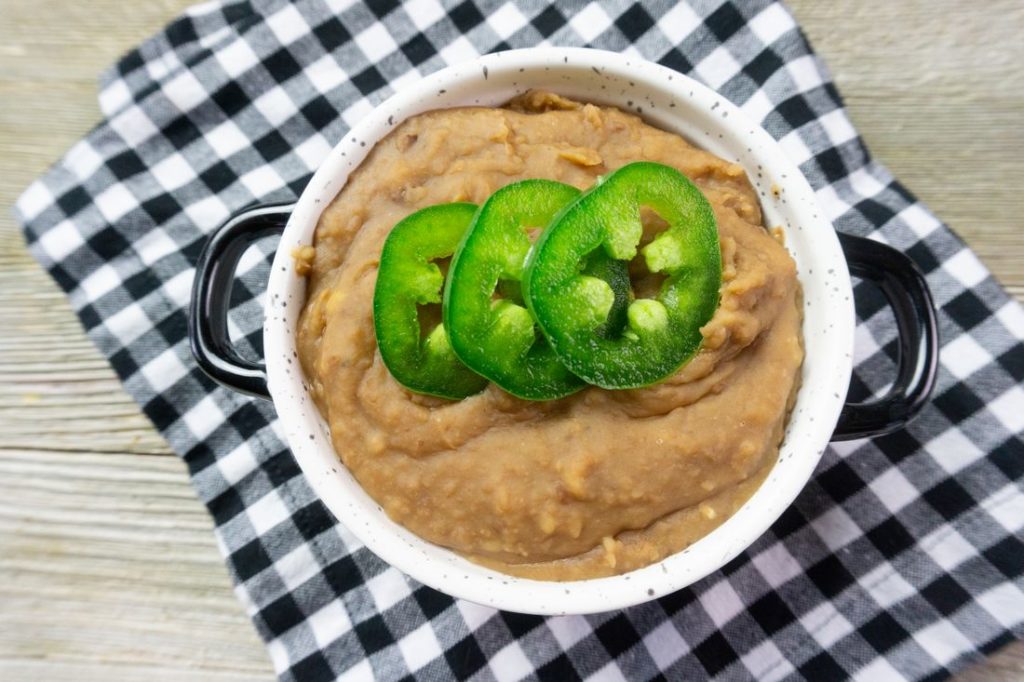 Instant Pot Refried Beans in a white bowl on plaid napkin on grey wood.