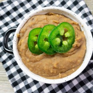 Instant Pot Refried Beans in a white bowl on plaid napkin on grey wood.