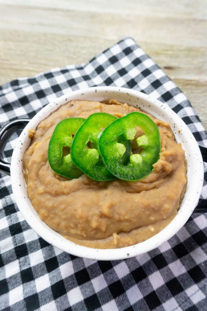 Instant Pot Refried Beans in a white bowl on plaid napkin on grey wood.