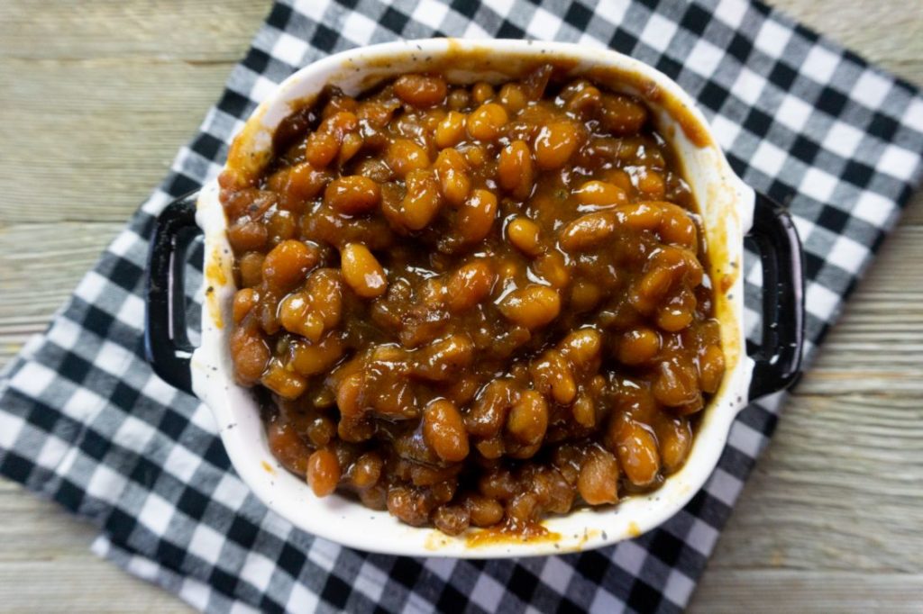 Instant Pot Baked Beans on a wood board in a black and white speckled bowl with black and white plaid napkin