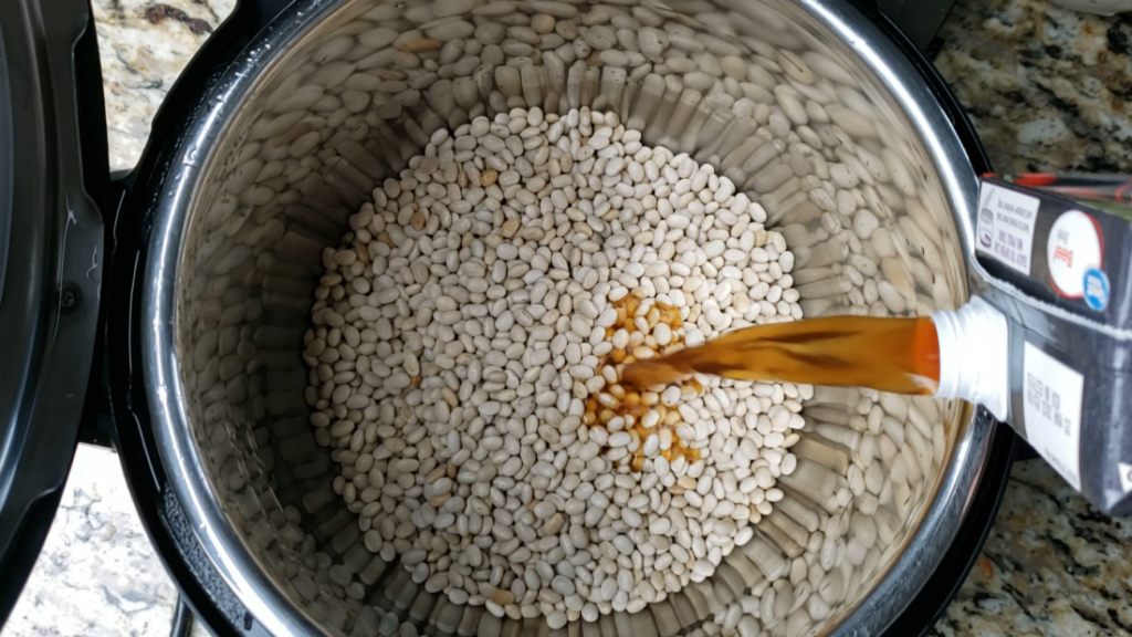 white beans inside the instant pot with beef broth pouring in