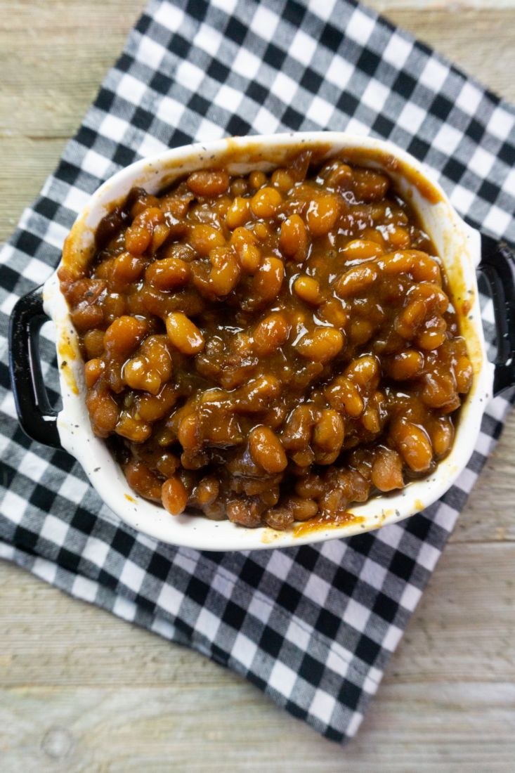 Instant Pot Baked Beans on a wood board in a black and white speckled bowl with black and white plaid napkin