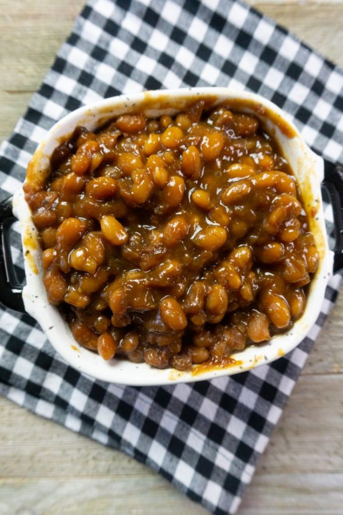 Instant Pot Baked Beans on a wood board in a black and white speckled bowl with black and white plaid napkin