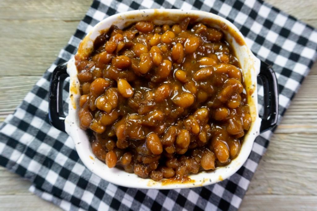 Instant Pot Baked Beans on a wood board in a black and white speckled bowl with black and white plaid napkin