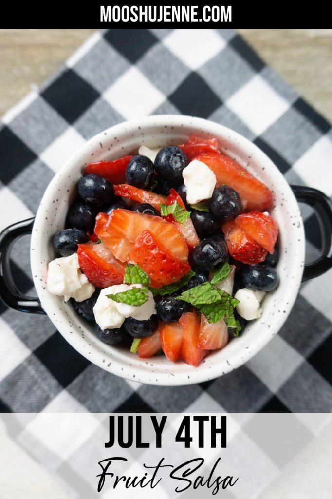 July 4th Fruit Salad with strawberries, blueberries, and mozzarella pearl cheese in a whote bowl with black speckles on a black and white plaid napkin