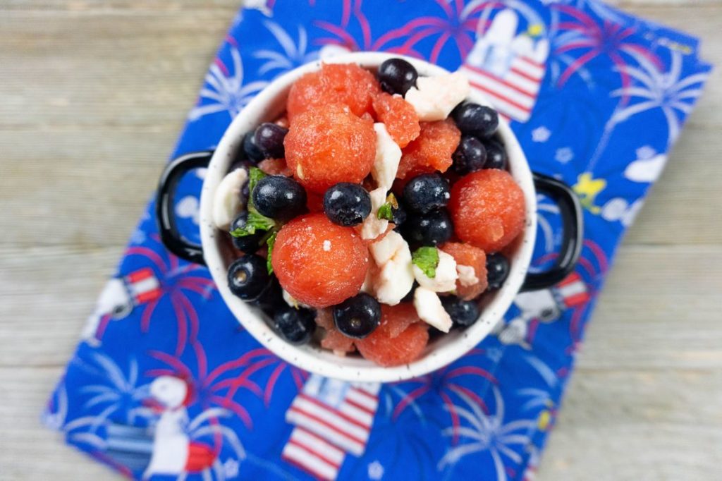 Watermelon, pearl mozzarella, blueberries, and mint in a white bowl on a snoopy cloth napkin